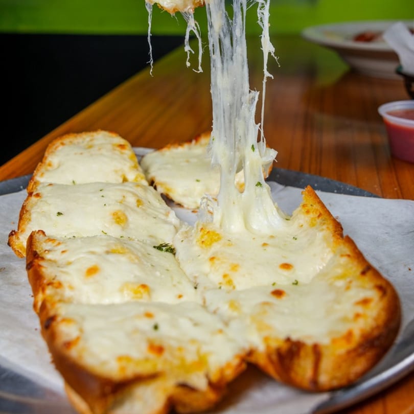 Cheesy garlic bread with melted mozzarella stretching upwards, served on a tray at Mama's Pizza & Grill.