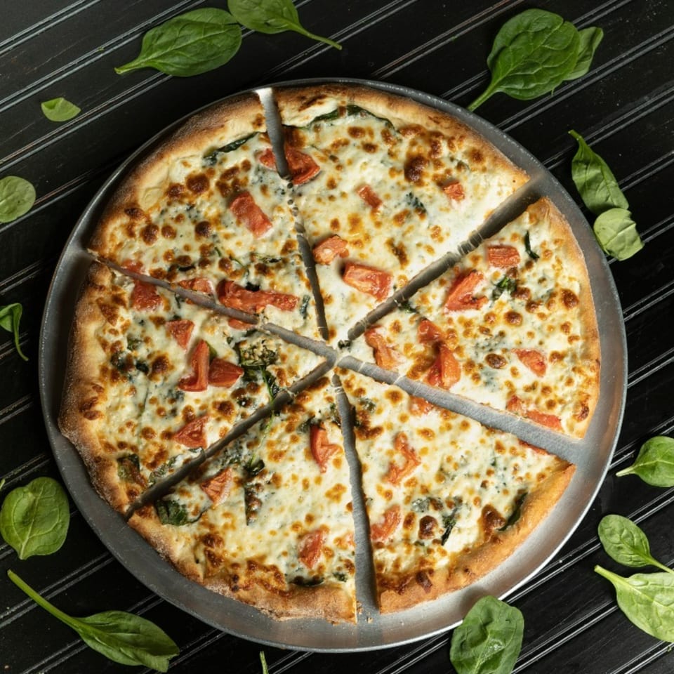 Mama's Pizza & Grill's sliced white pizza with tomatoes and spinach on a dark background.