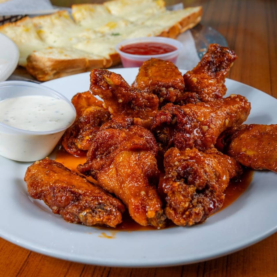 A plate of Mama's Pizza & Grill's saucy chicken wings with ranch, ketchup, and cheesy bread.