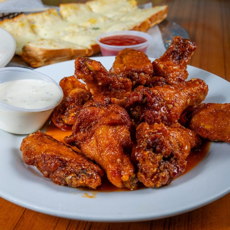 A plate of Mama's Pizza & Grill's saucy chicken wings with ranch, ketchup, and cheesy bread.
